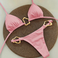 Pink bikini set with gold straps on a textured brown mat