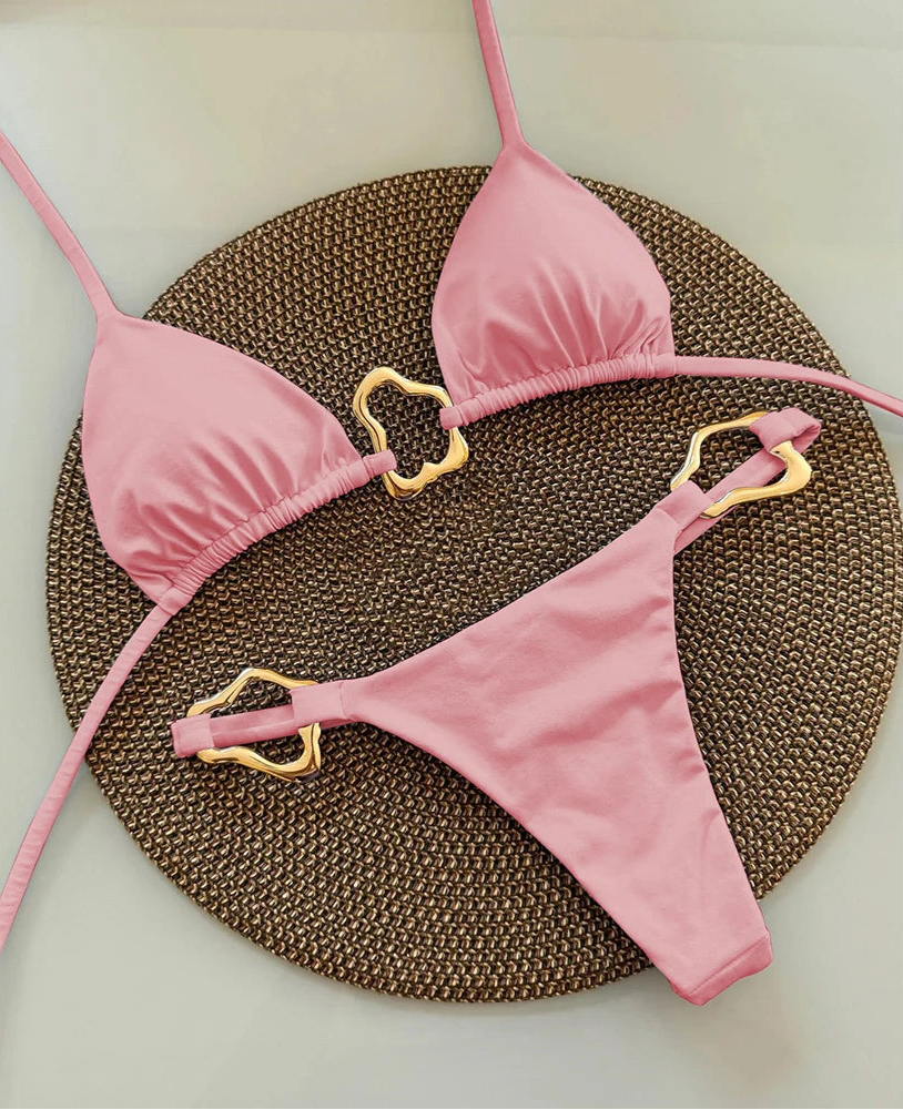 Pink bikini set with gold straps on a textured brown mat