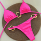 Pink bikini set with gold heart-shaped straps on a textured brown surface
