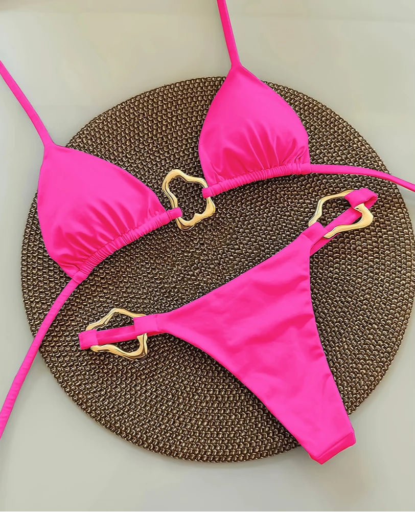 Pink bikini set with gold heart-shaped straps on a textured brown surface