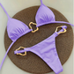 Purple bikini set with gold heart-shaped straps on a textured brown mat