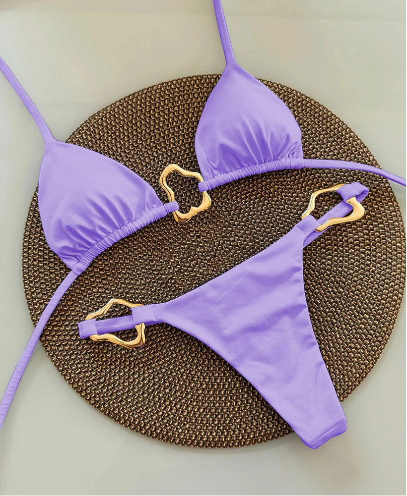 Purple bikini set with gold heart-shaped straps on a textured brown mat
